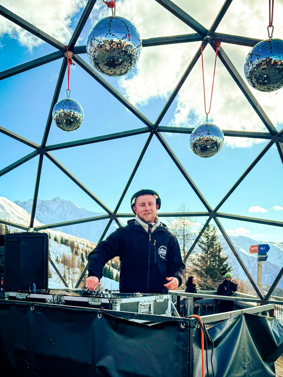 NATUS DJing beneath disco balls in a glass dome overlooking snowy mountains